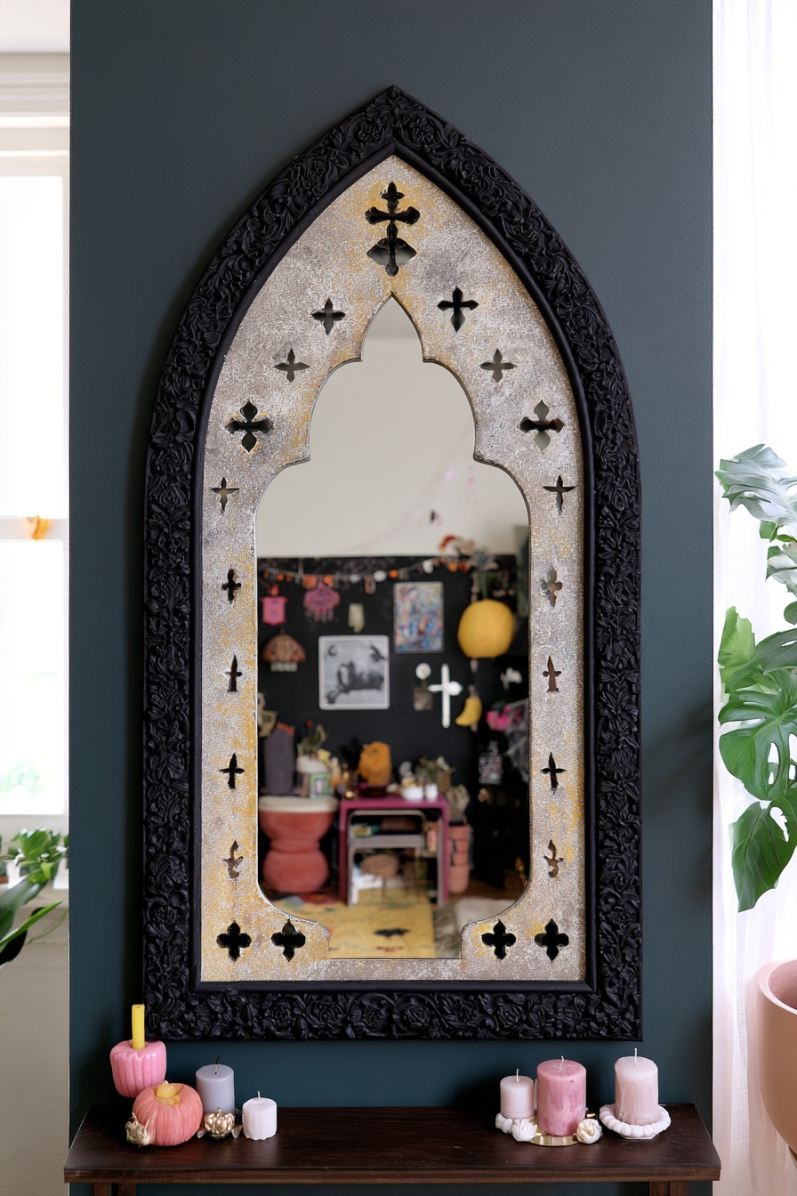 Tall pointed black mirror with a gold inner border on a deep teal wall above a slim wood console
