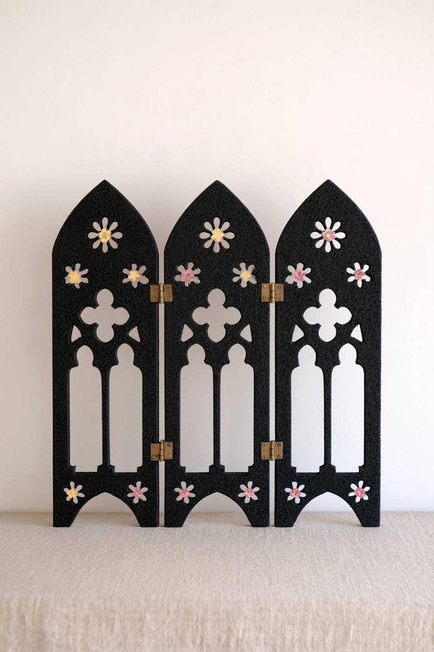 Three black hinged tabletop panels with pointed arches, open tracery, and small pink and cream flowers