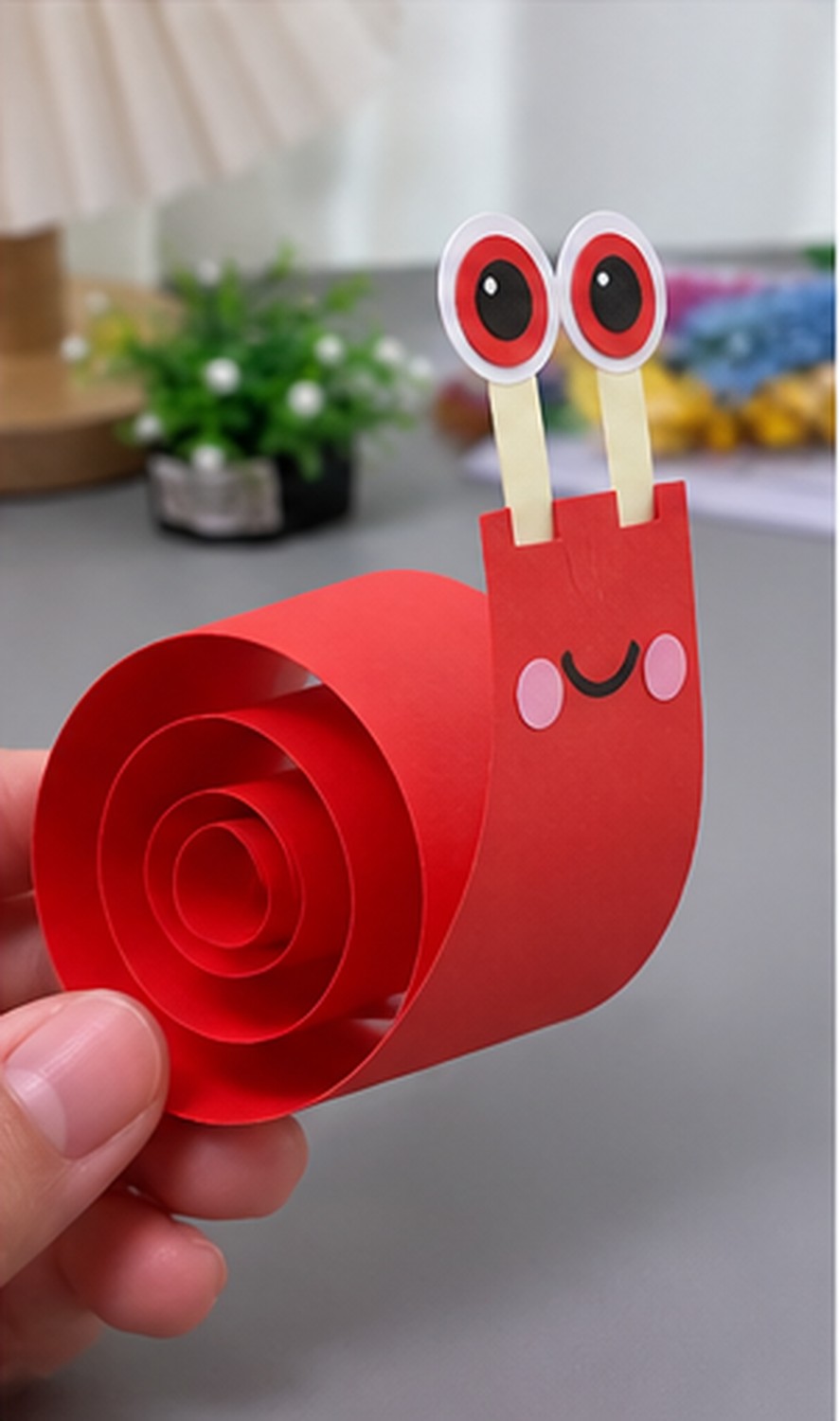 Red paper snail with an upright face and a rolled spiral shell before the white spots are attached