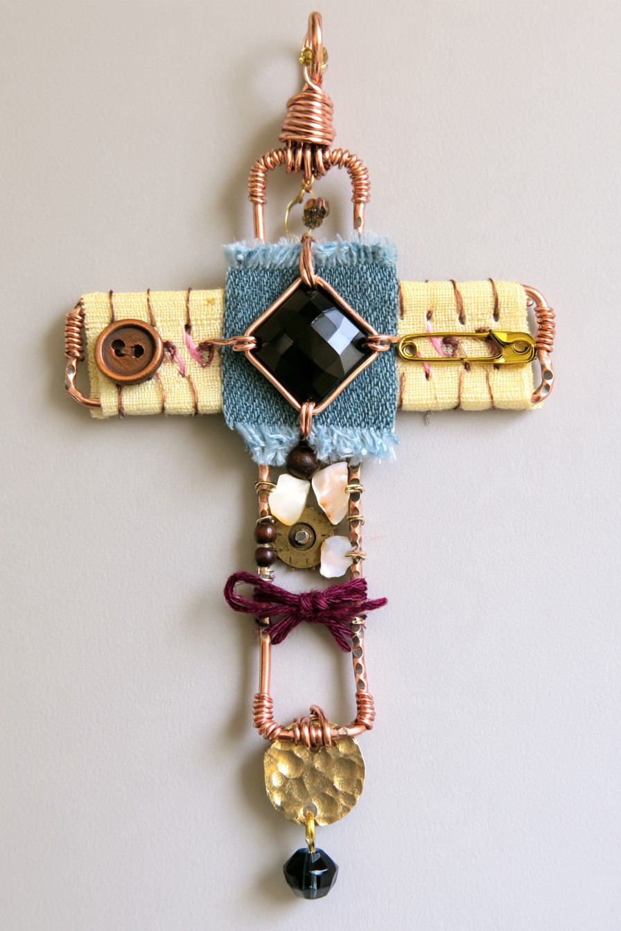Textile cross pendant with black crystal and sewing-inspired accents