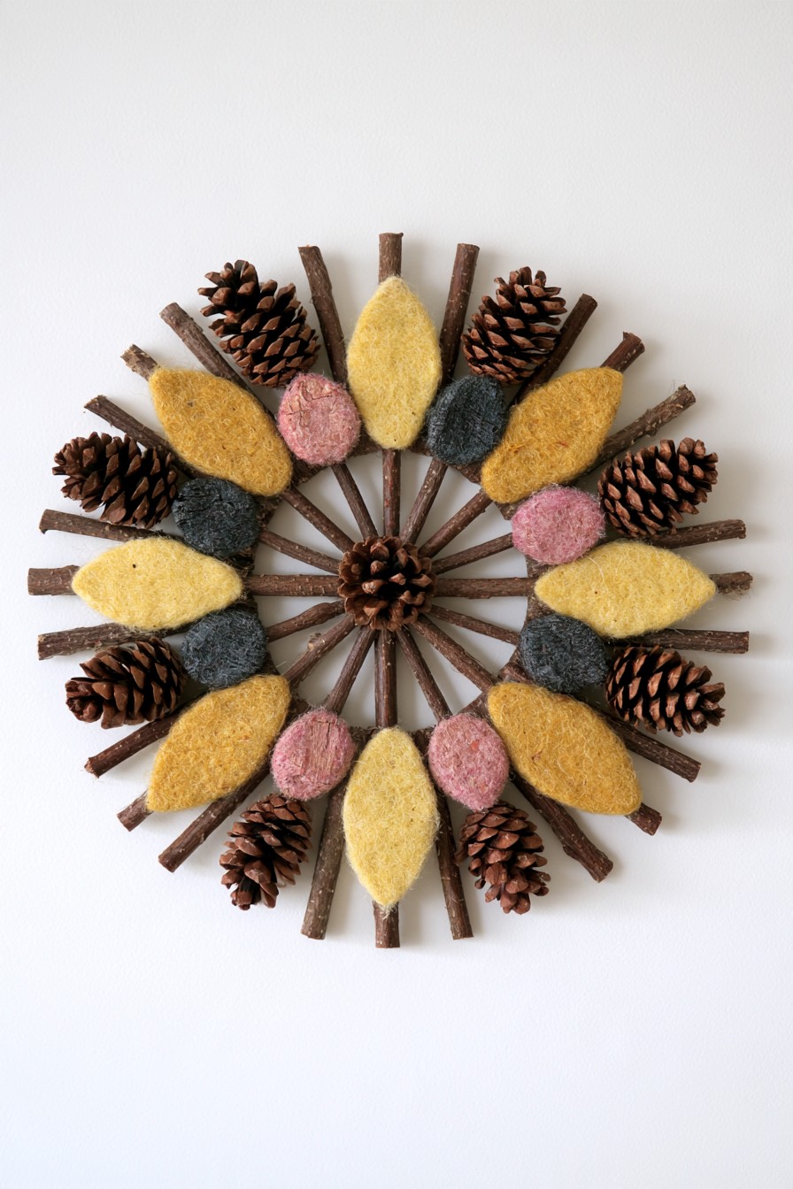 Radial wall decoration made from twigs, pinecones, and felted leaf shapes