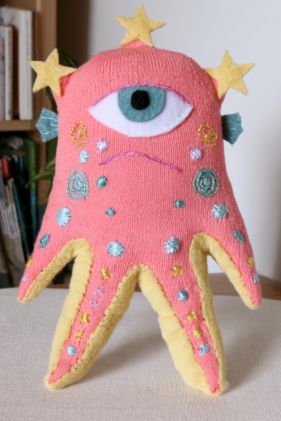 Coral pink starfish alien character with one large turquoise eye, yellow edging and soft lower points