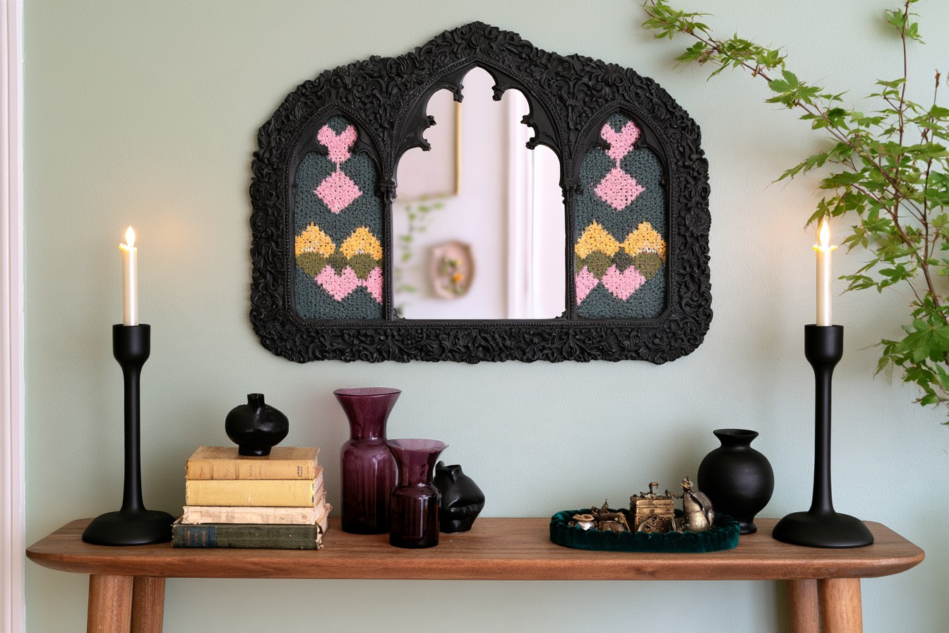 Wide black arched mirror with pink and mustard patterned side panels above a wood console and plum glass vases