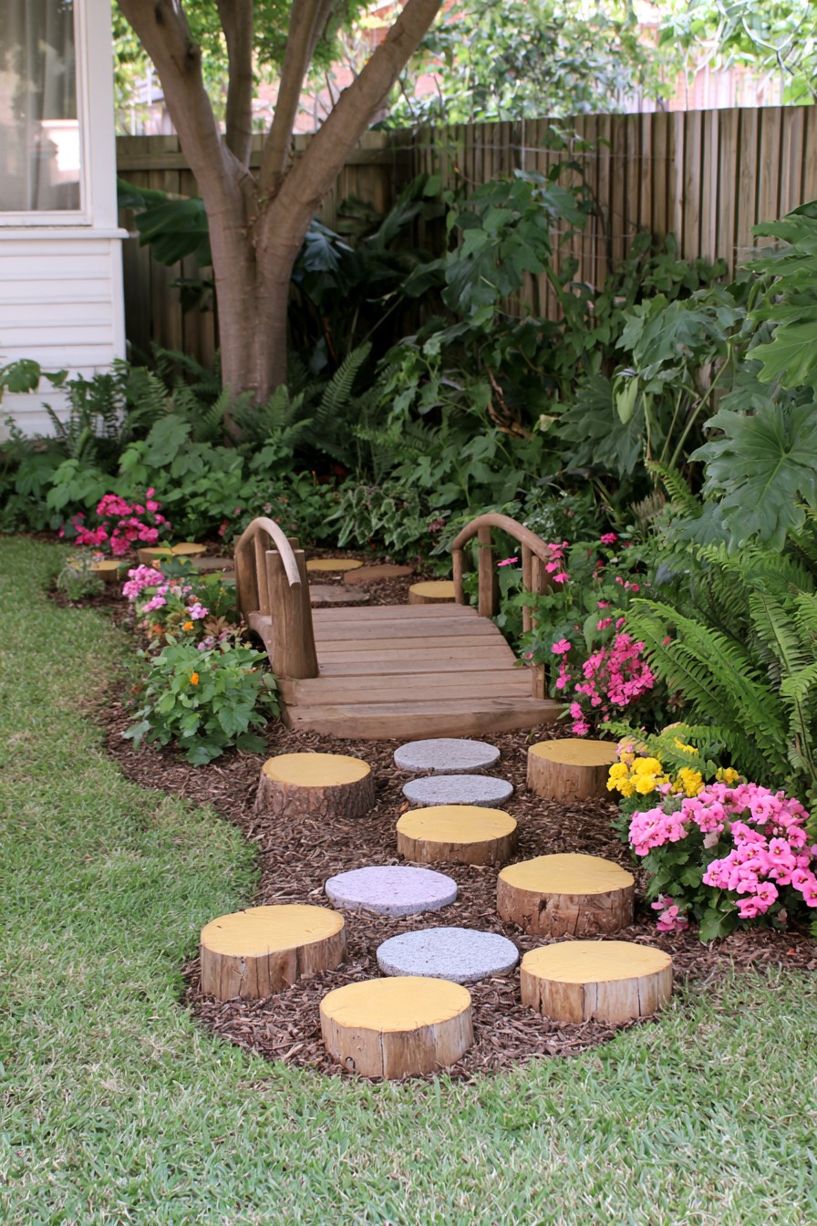 Garden balance trail with log stepping posts leading toward a small timber bridge