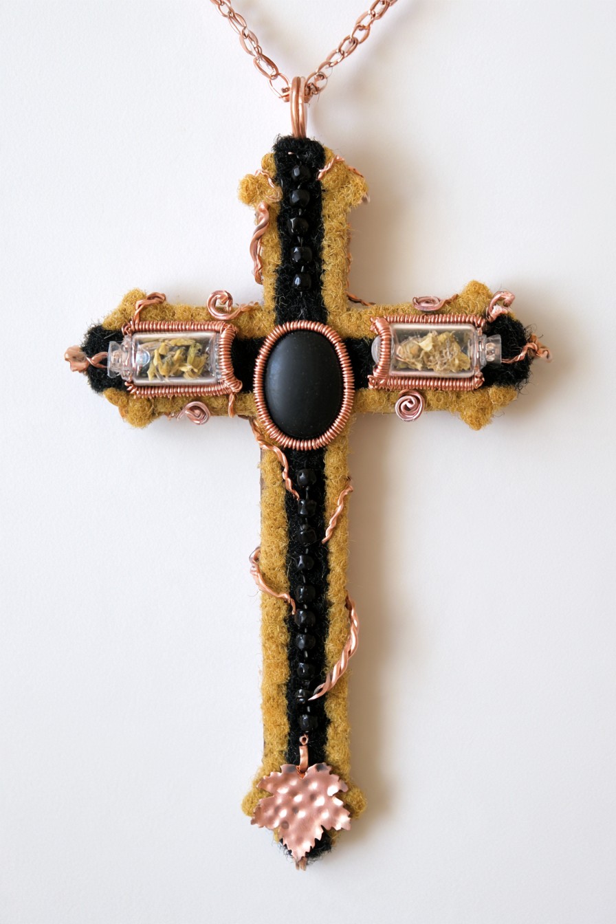Mustard textile cross with clear floral compartments, a black oval center and copper-colored wire