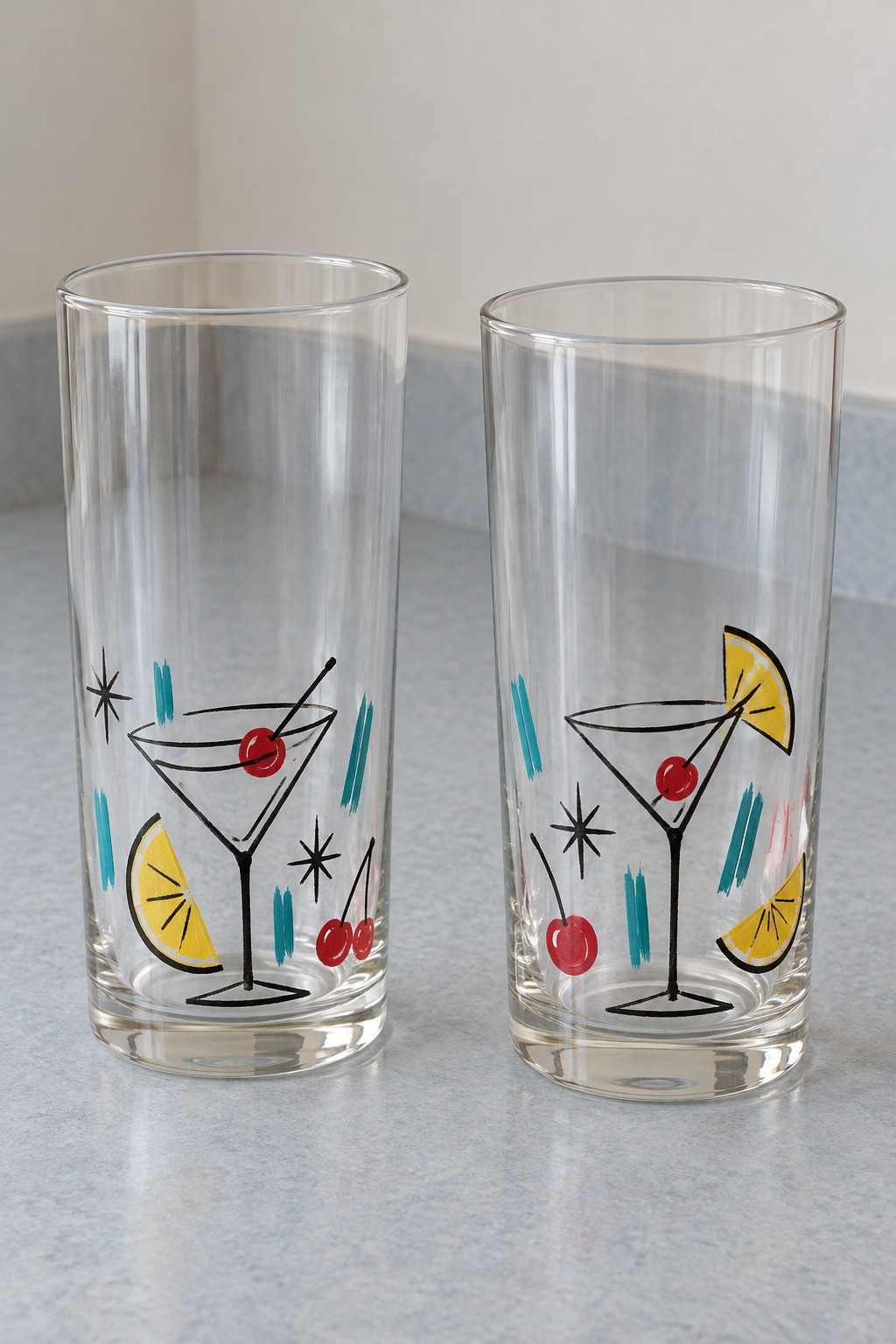 Tall clear glasses painted with cocktail bowls, red cherries, yellow citrus and black starbursts