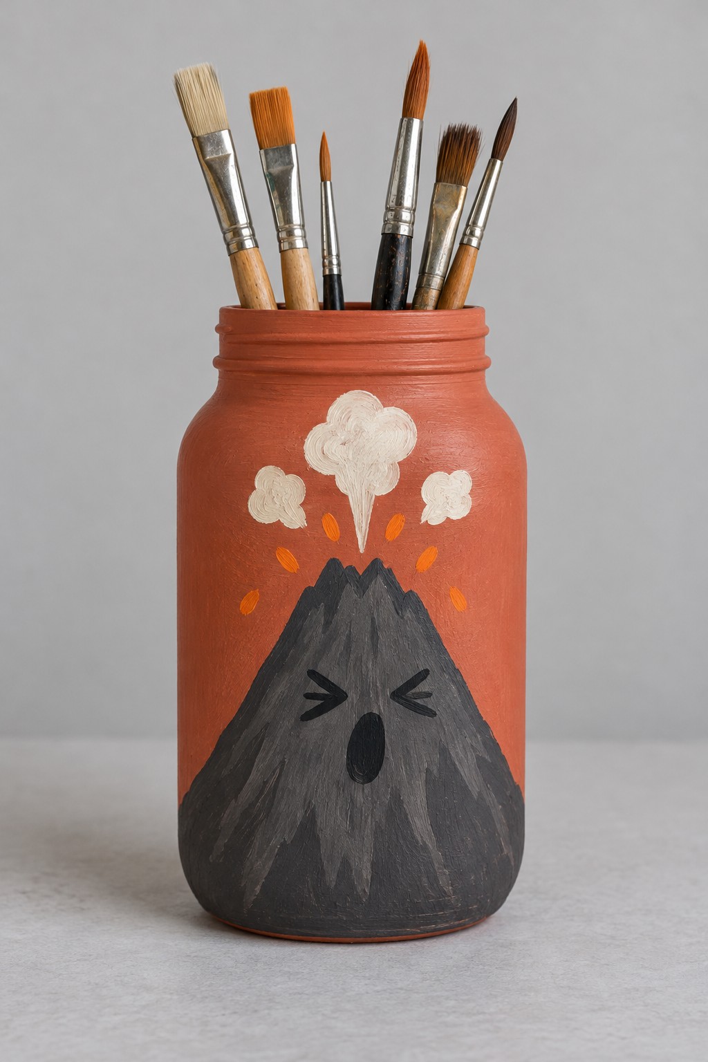 Terracotta orange jar with a dark gray expressive volcano and cream painted smoke holding paintbrushes