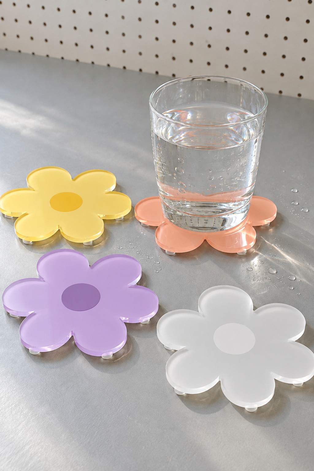 Yellow pink lilac and white acrylic daisy coasters with a glass of water