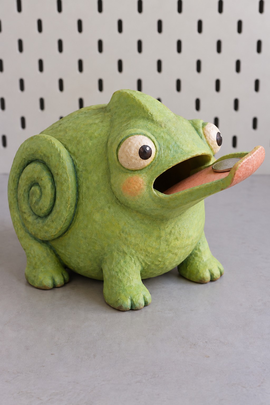 Green chameleon coin bank with raised eyes, curled tail and a pink tongue leading into its mouth