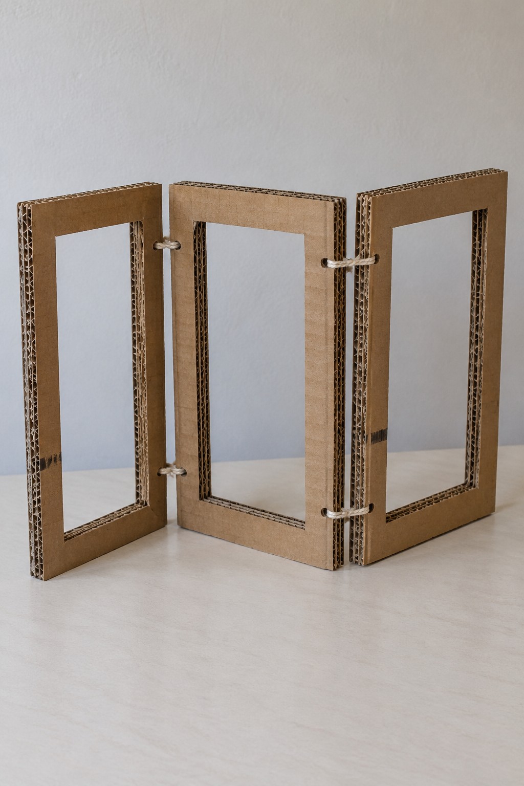 Three open rectangular corrugated cardboard panels connected with cord hinges as a small folding screen
