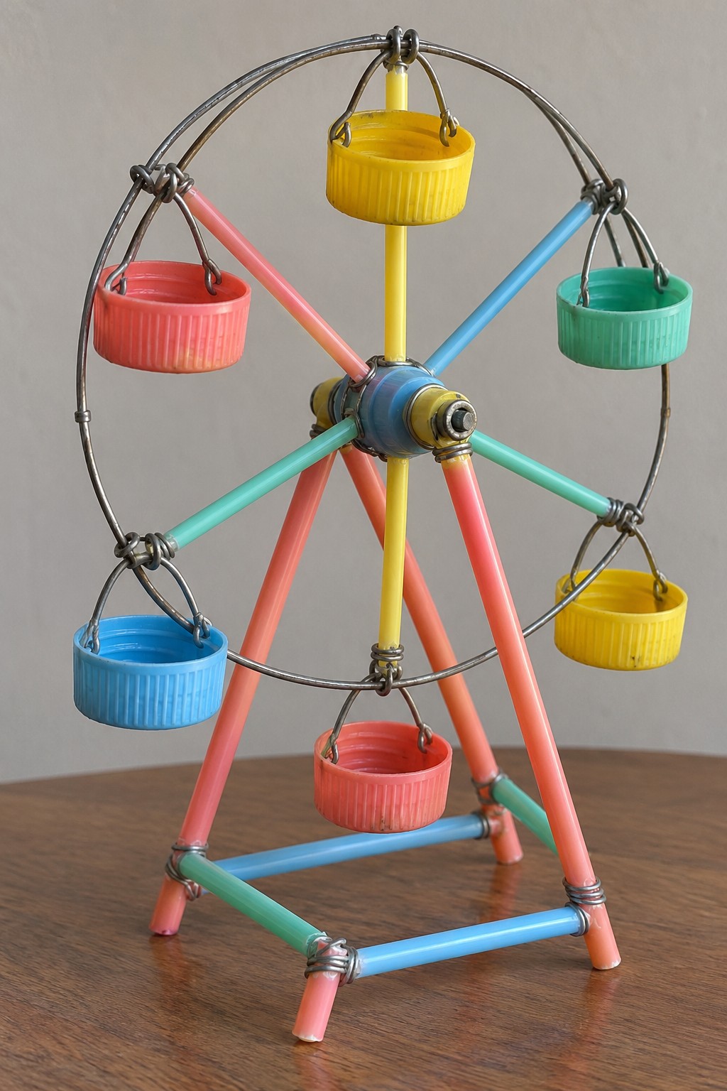 Colorful miniature Ferris wheel with six bottle cap gondolas a wire rim and a braced straw stand