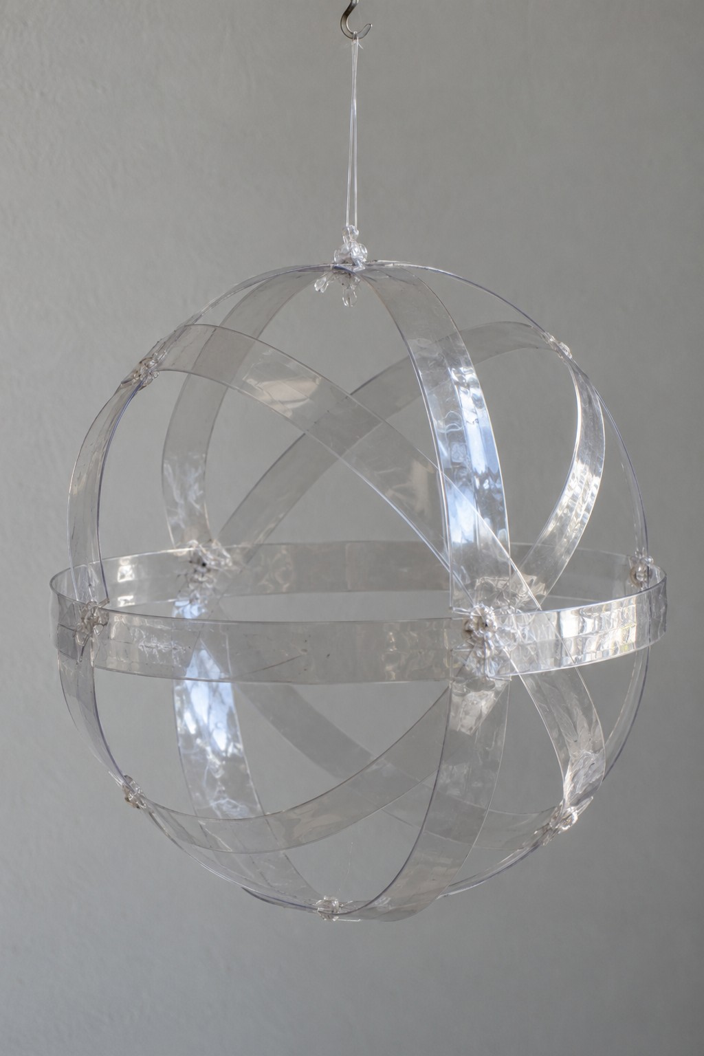 Hanging open sphere assembled from clear plastic strips with visible connections at the intersections