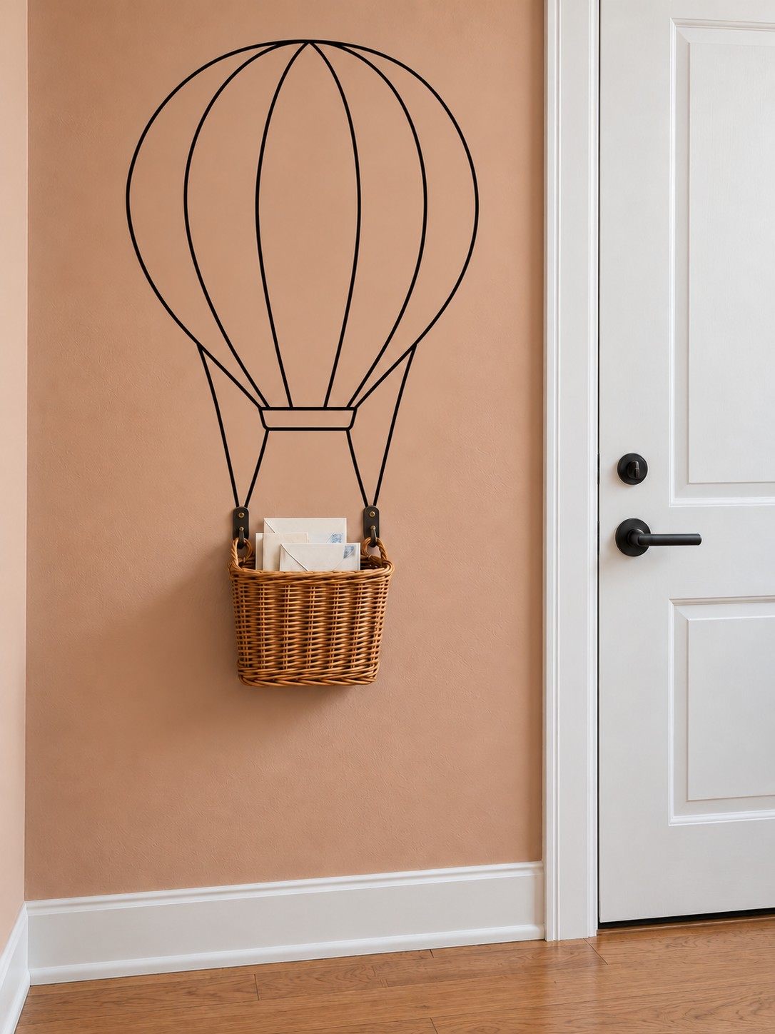 Wicker wall basket holding mail beneath a black hot air balloon outline on a peach wall