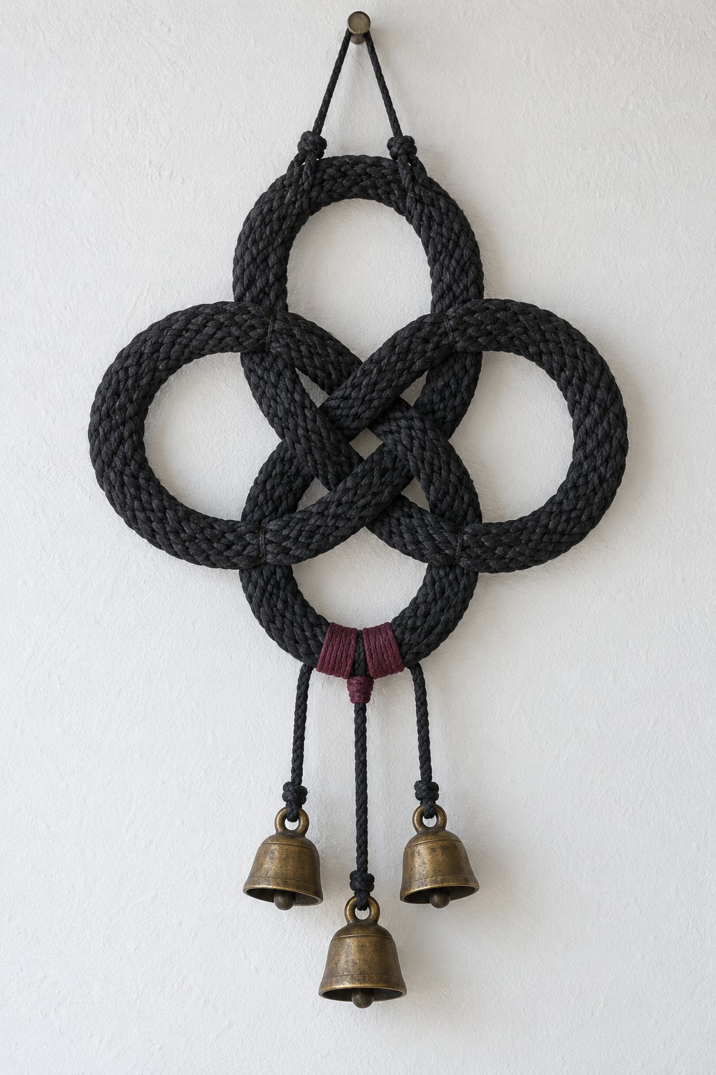 Four lobed black rope wall motif with plum binding and three brass bells, the middle bell hanging lower