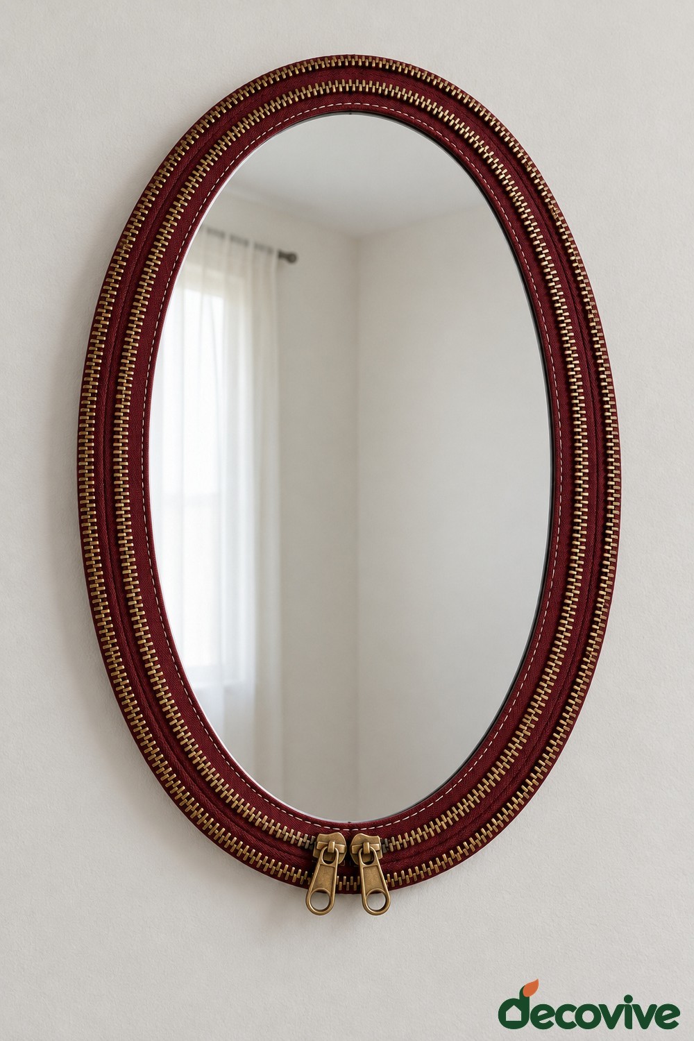 Burgundy oval mirror with brass colored zipper teeth and two zipper pulls at the bottom