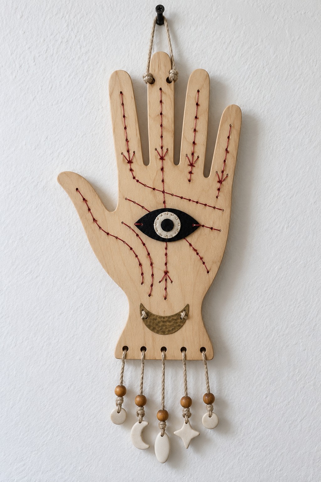 Pale wooden hand with burgundy stitched lines, a central black eye, a brass colored crescent and small dangling charms