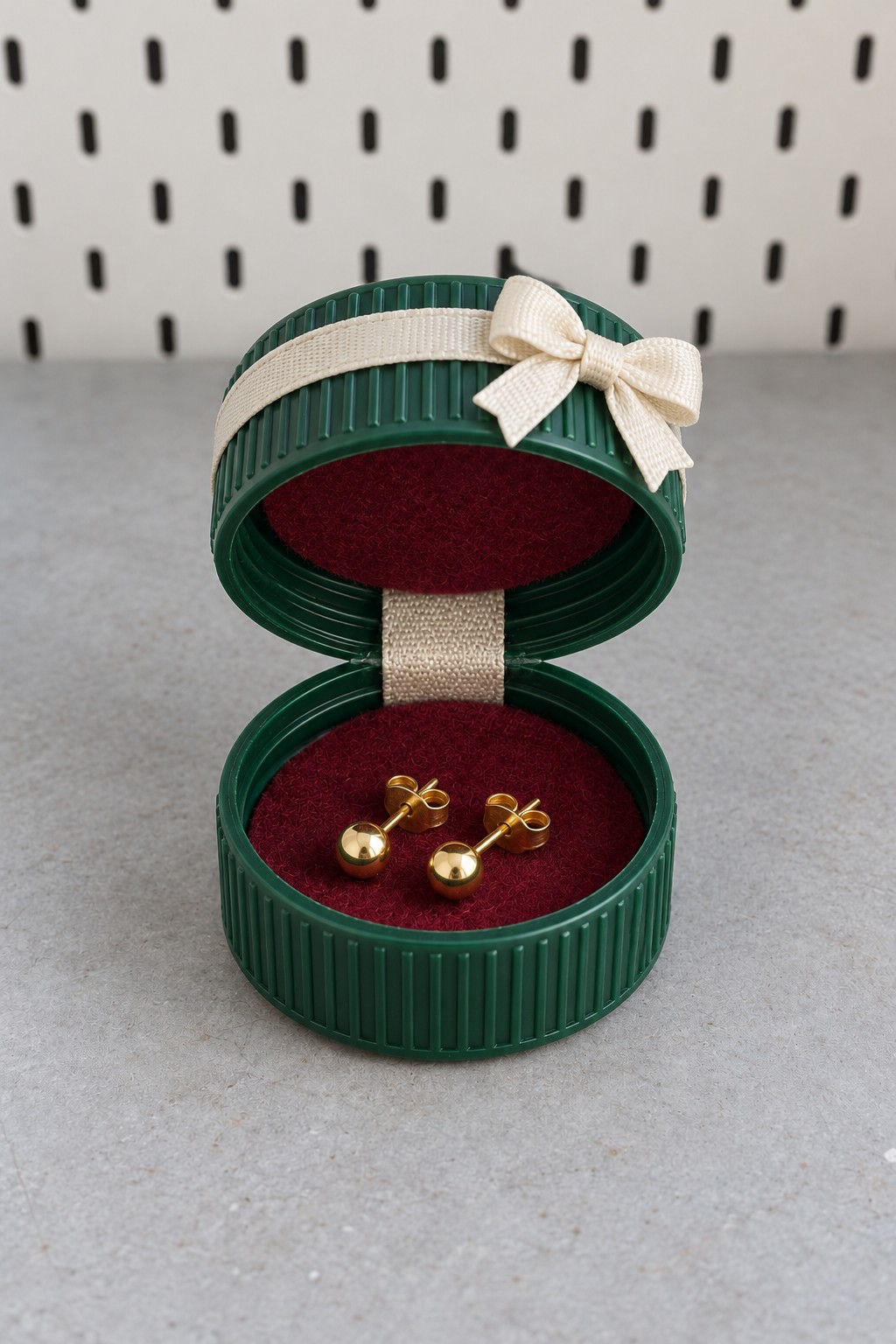 Small green two cap jewelry box with burgundy velvet lining, cream ribbon hinge, and bow holding gold earrings