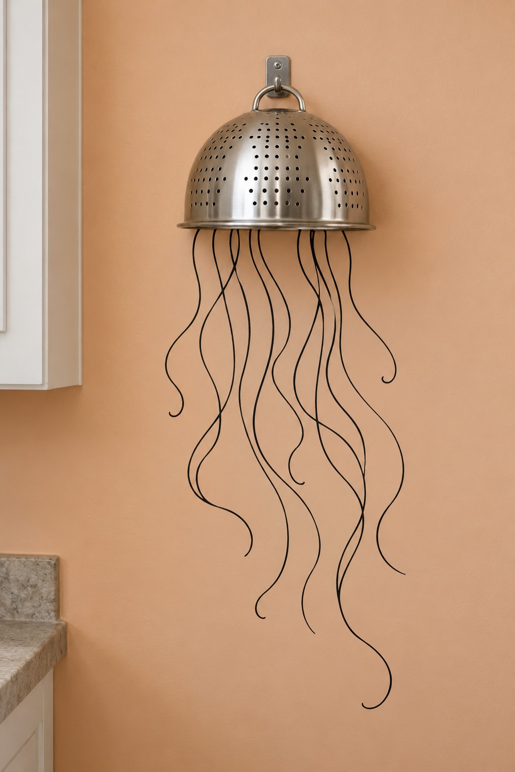 Inverted metal colander hanging above flowing black jellyfish tentacles on a warm orange wall