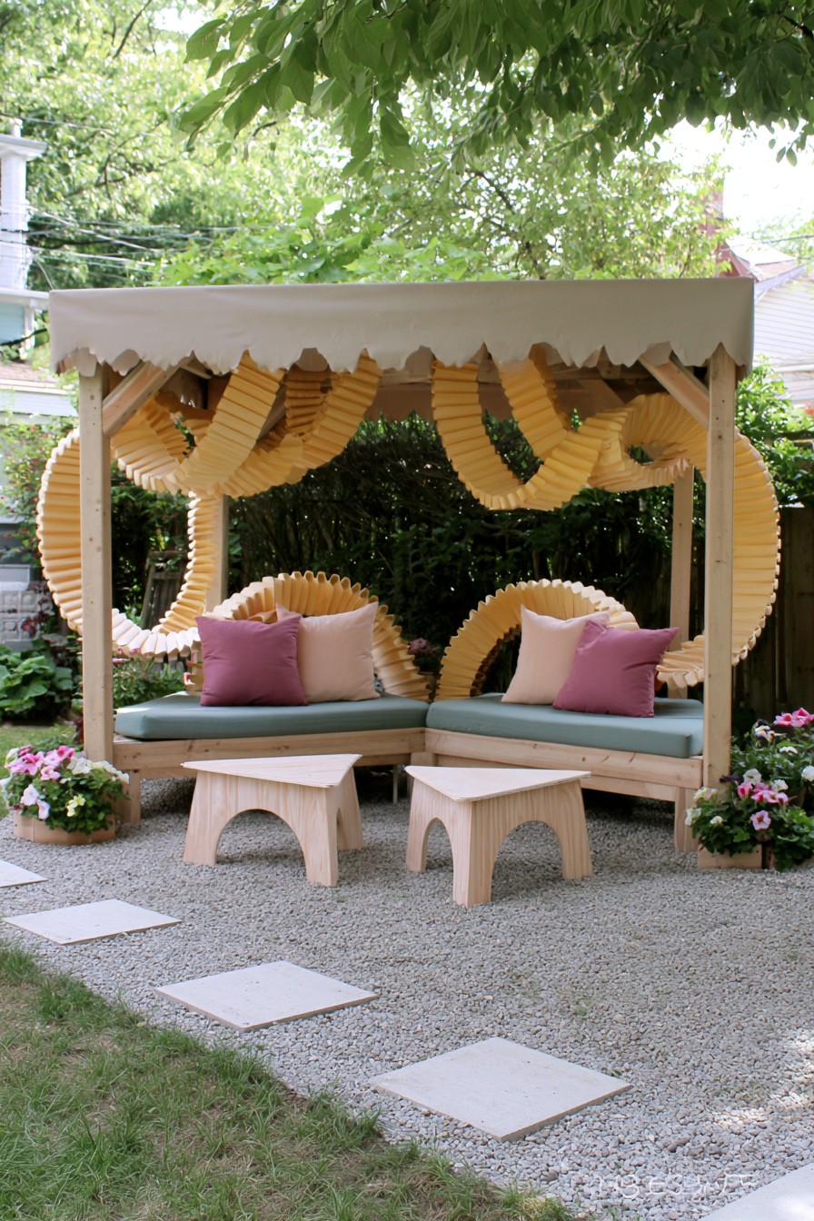 Yellow accordion-folded loops behind paired benches and two pale wooden tables