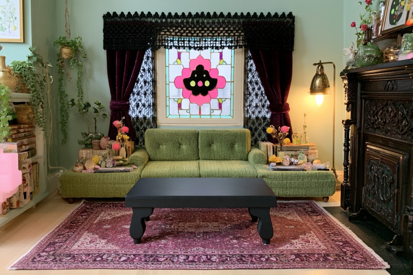Low olive sofa beneath a floral colored glass panel, with burgundy curtains, black lace, and a carved dark fireplace surround