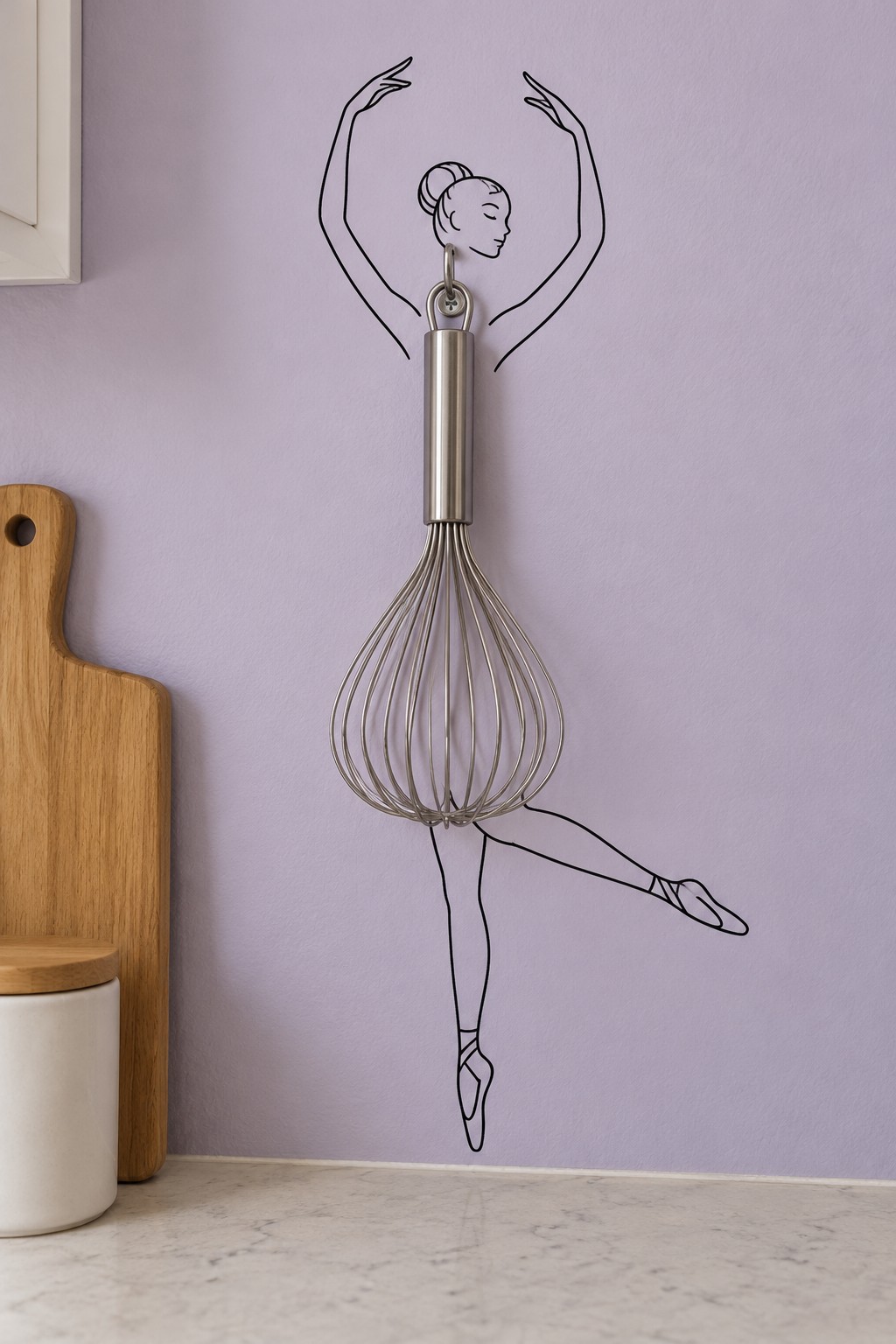 Metal balloon whisk hanging over a ballerina outline so its wire loops form a tutu on a lavender wall