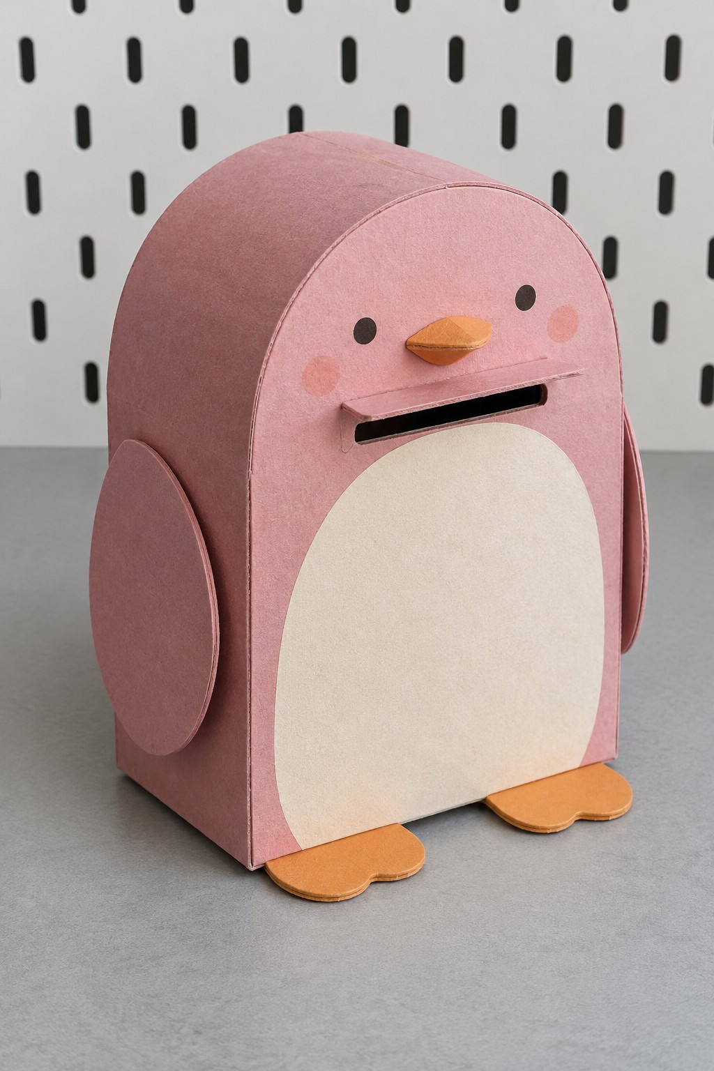 Pink penguin coin bank with a cream belly, orange feet and a horizontal front coin slot