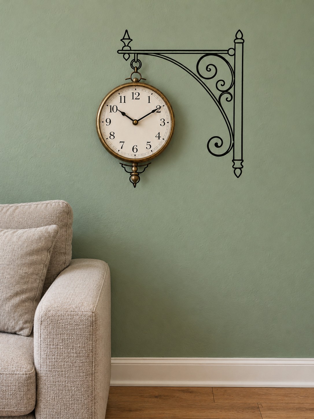 Brass wall clock aligned with a black painted ornamental bracket on a sage green wall