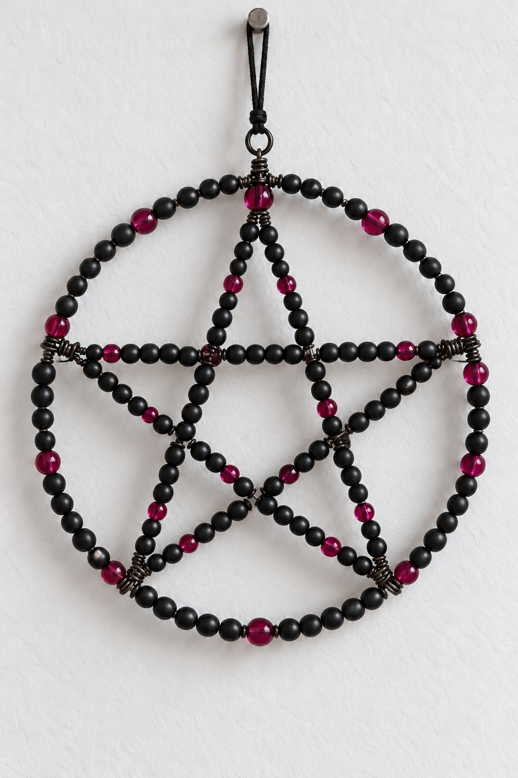 Round pentagram made with black beads and scattered berry pink beads on a dark wire structure
