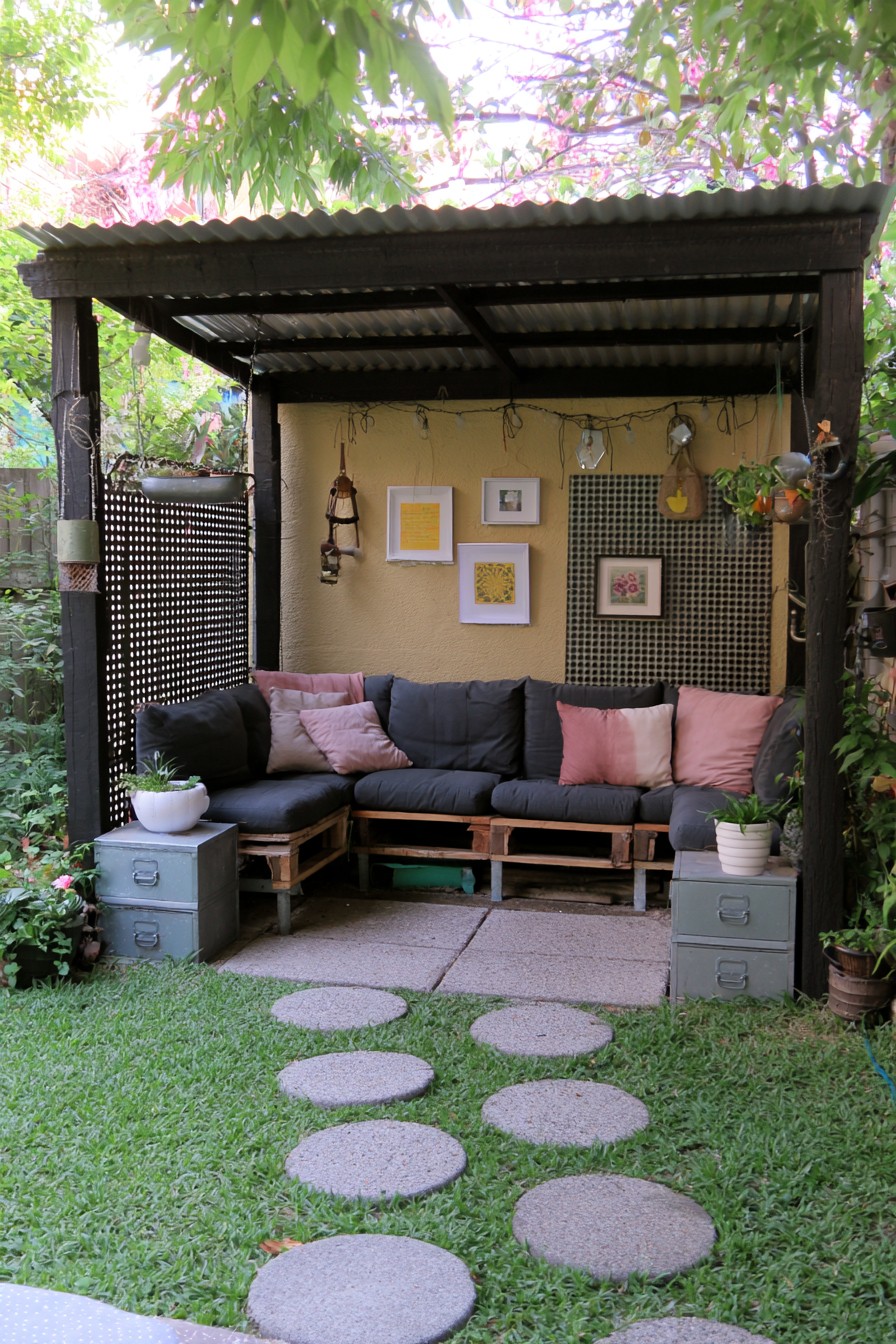Dark corrugated-roof lounge with pallet-style seating, pink cushions, and metal drawers