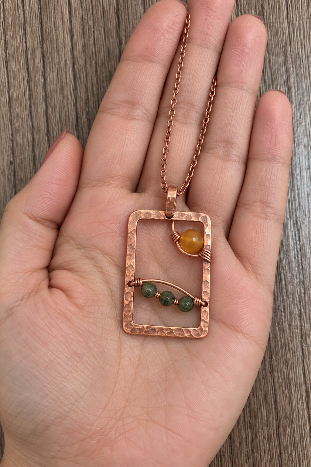 Rectangular hammered copper pendant with a golden bead and a curved row of green beads