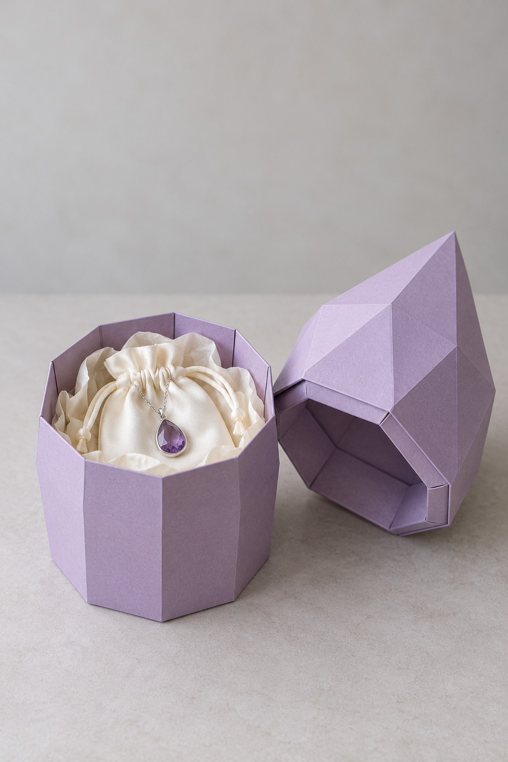Lavender geometric jewelry box with a faceted pointed lid and a cream pouch displaying a purple pendant