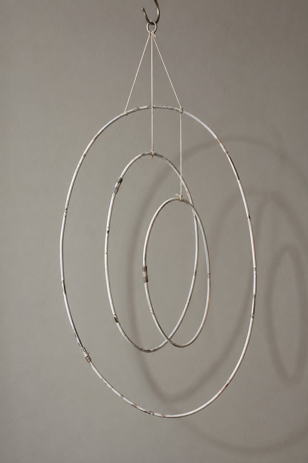 Three silver wire rings of decreasing size suspended inside one another on thin white cords