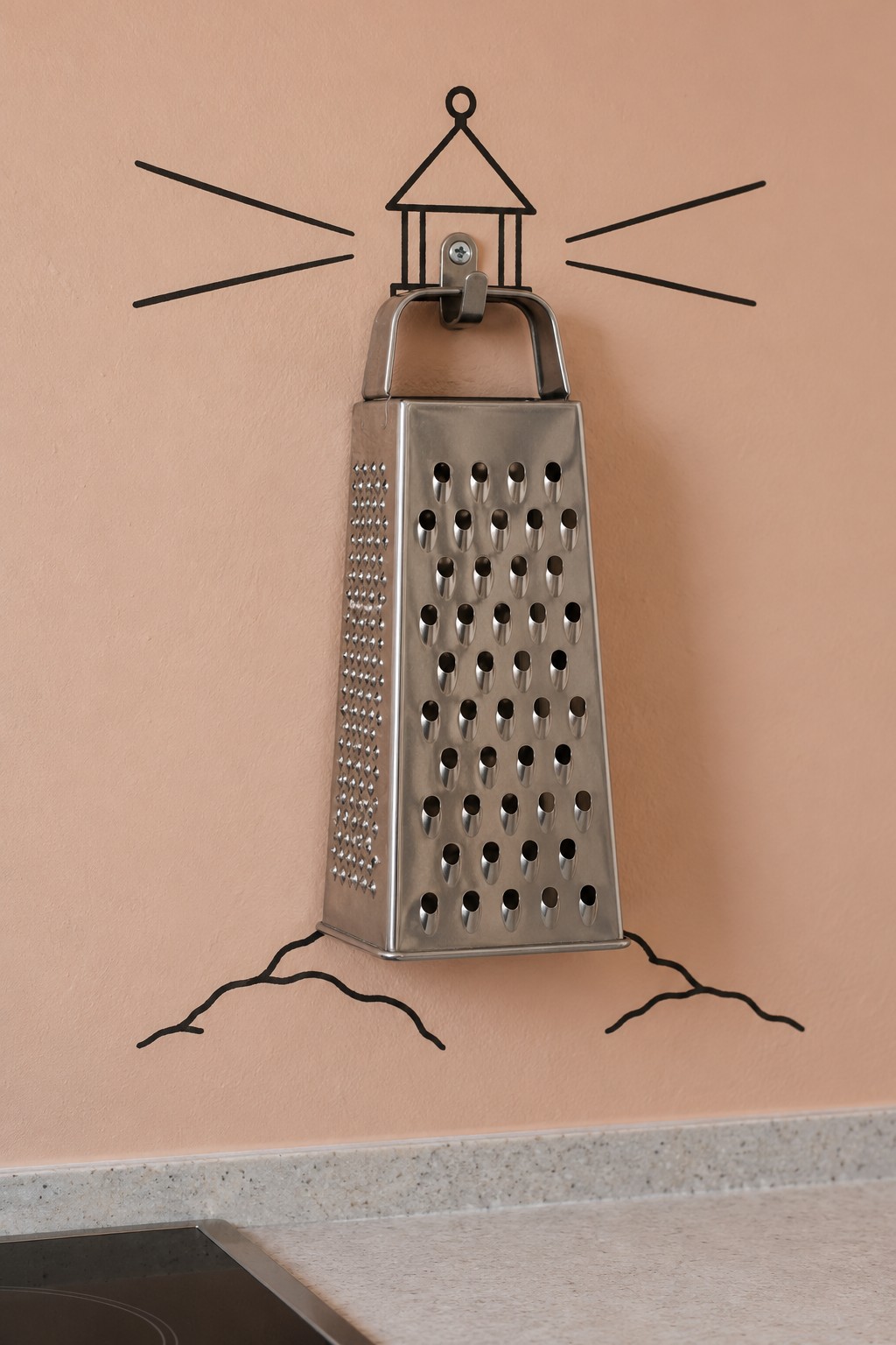 Metal box grater forming a lighthouse tower with a painted lantern, light beams and rocky base