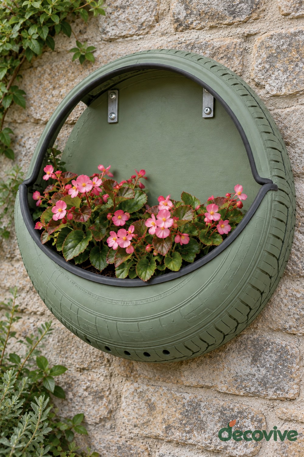 Sage green tire wall planter with a shaped upper opening, matching backing, and pink begonias in its lower pocket