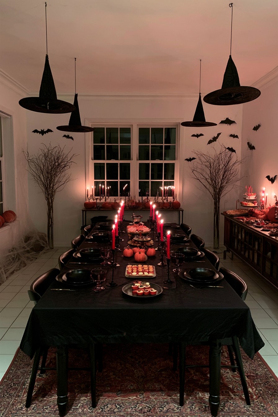 Suspended black witch hats and wall bats above a dark dining table with orange pumpkins