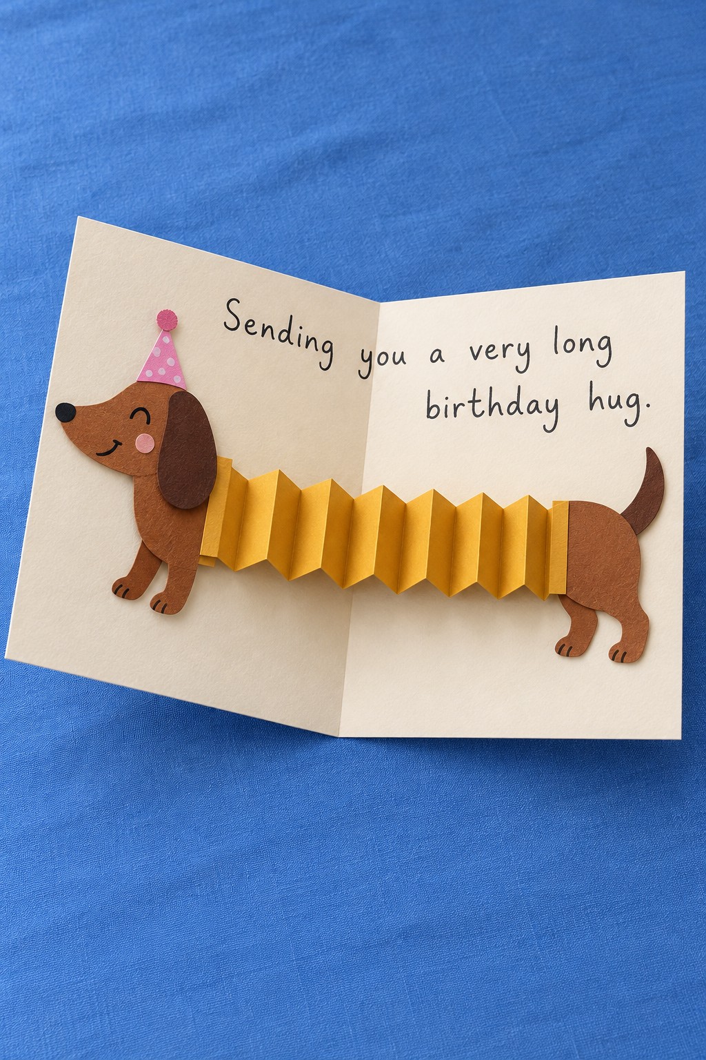 Open cream birthday card with a brown dachshund joined by a yellow accordion body