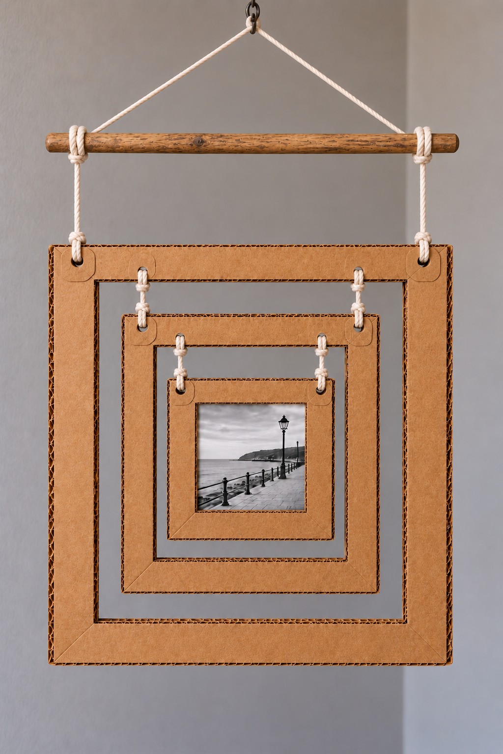 Three nested cardboard square frames suspended from a wooden dowel with a small monochrome photograph at the center