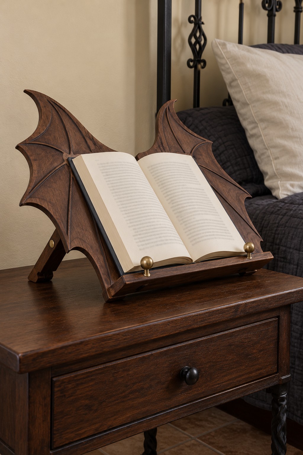 Dark wooden bookstand with two raised dragon wing shapes supporting an open book on a bedside table