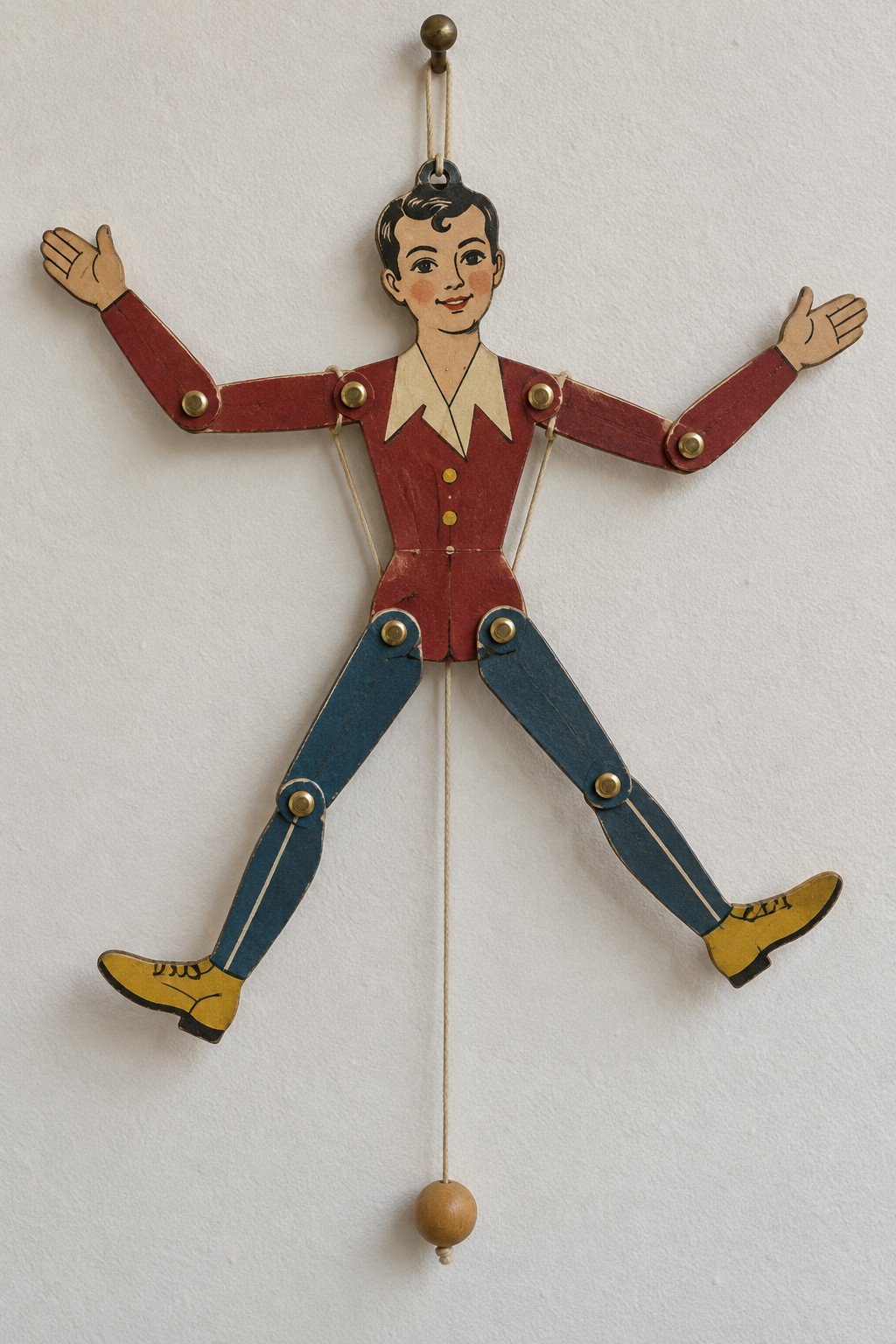 Jointed paper figure in a red jacket and blue trousers with a hanging pull cord