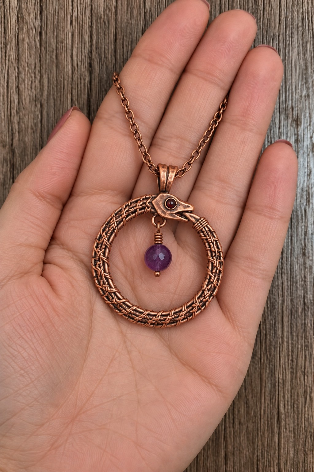 Circular woven copper snake pendant with its head meeting its tail and a purple bead hanging inside