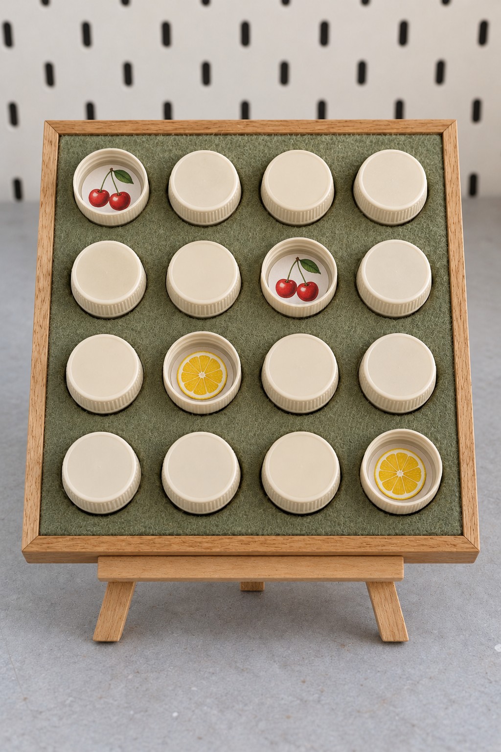 Sixteen cream plastic caps on a green felt board with two cherry pairs and lemon pictures revealed inside four caps
