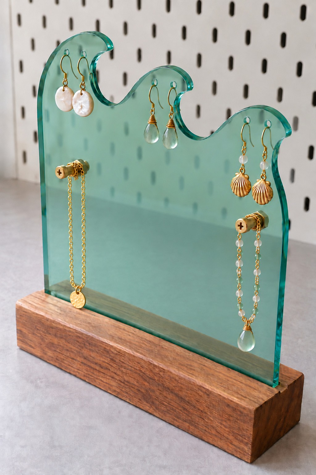 Sea green acrylic wave jewelry stand with earrings and necklaces above a walnut base