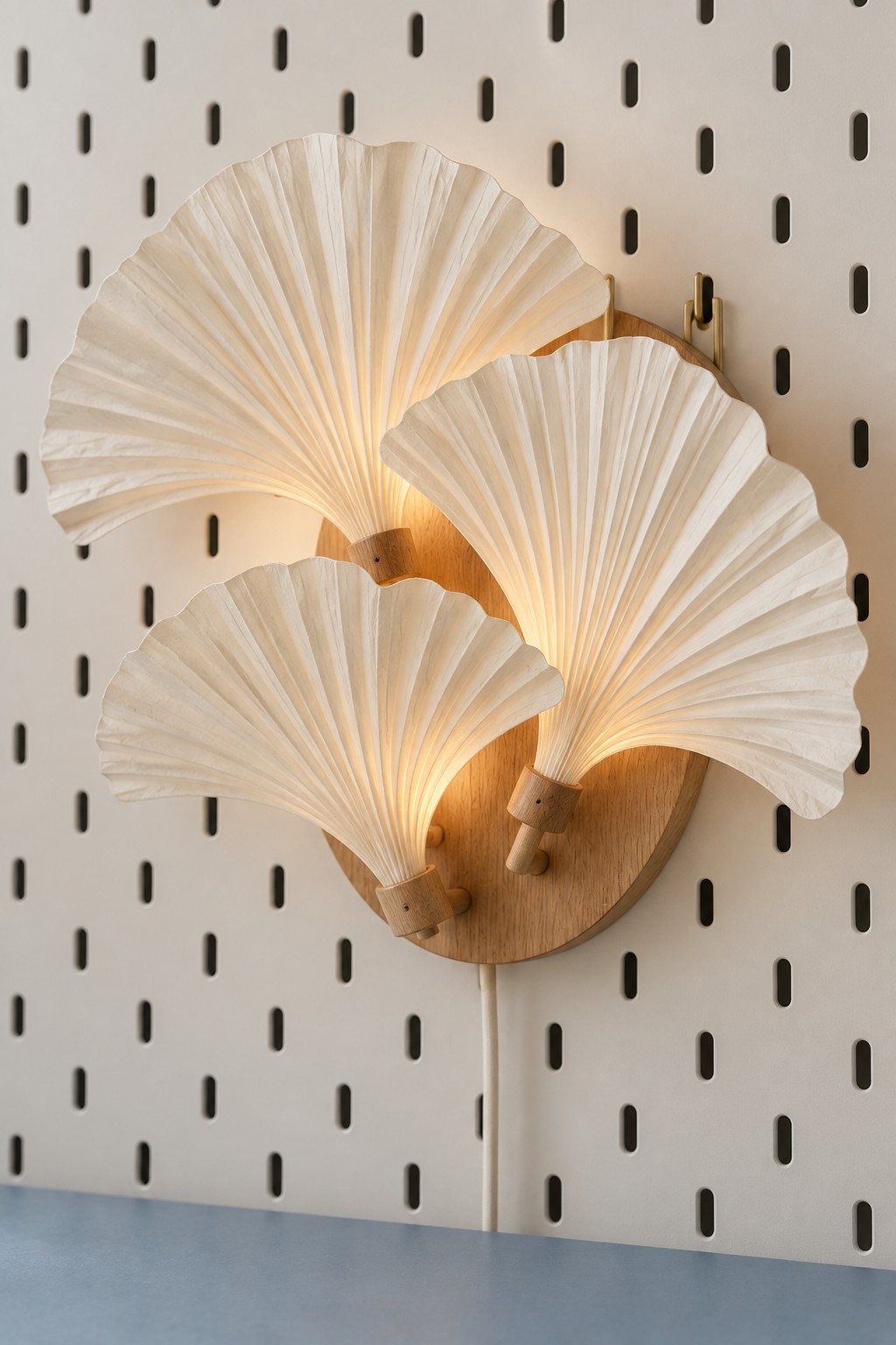 Three ivory pleated paper leaf fans on a round wooden wall light backplate