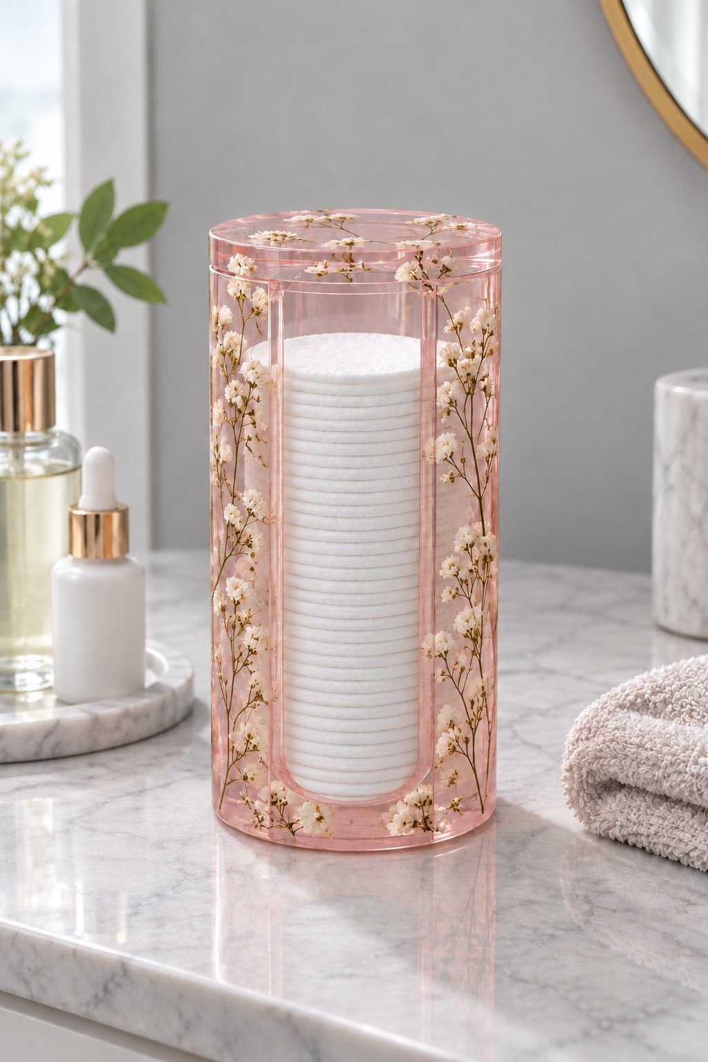 A tall clear pink resin cotton pad canister with small dried flowers, a matching lid and a stack of white cotton rounds.