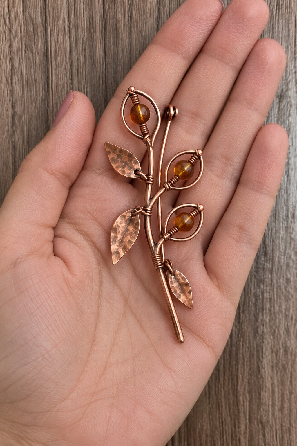 Copper branch brooch with hammered leaves and three amber colored beads in wire outlines