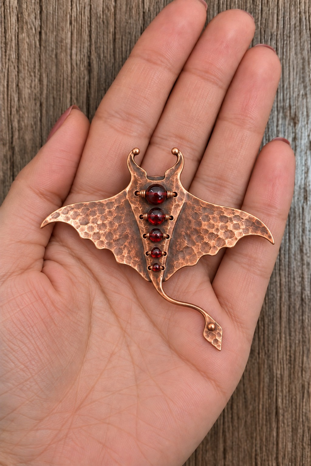 Wide hammered copper manta ray brooch with five graduated red beads and a curved tail