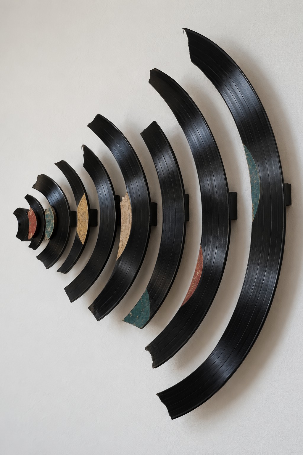 Black vinyl record arcs arranged from small to large on wall spacers with portions of faded labels visible