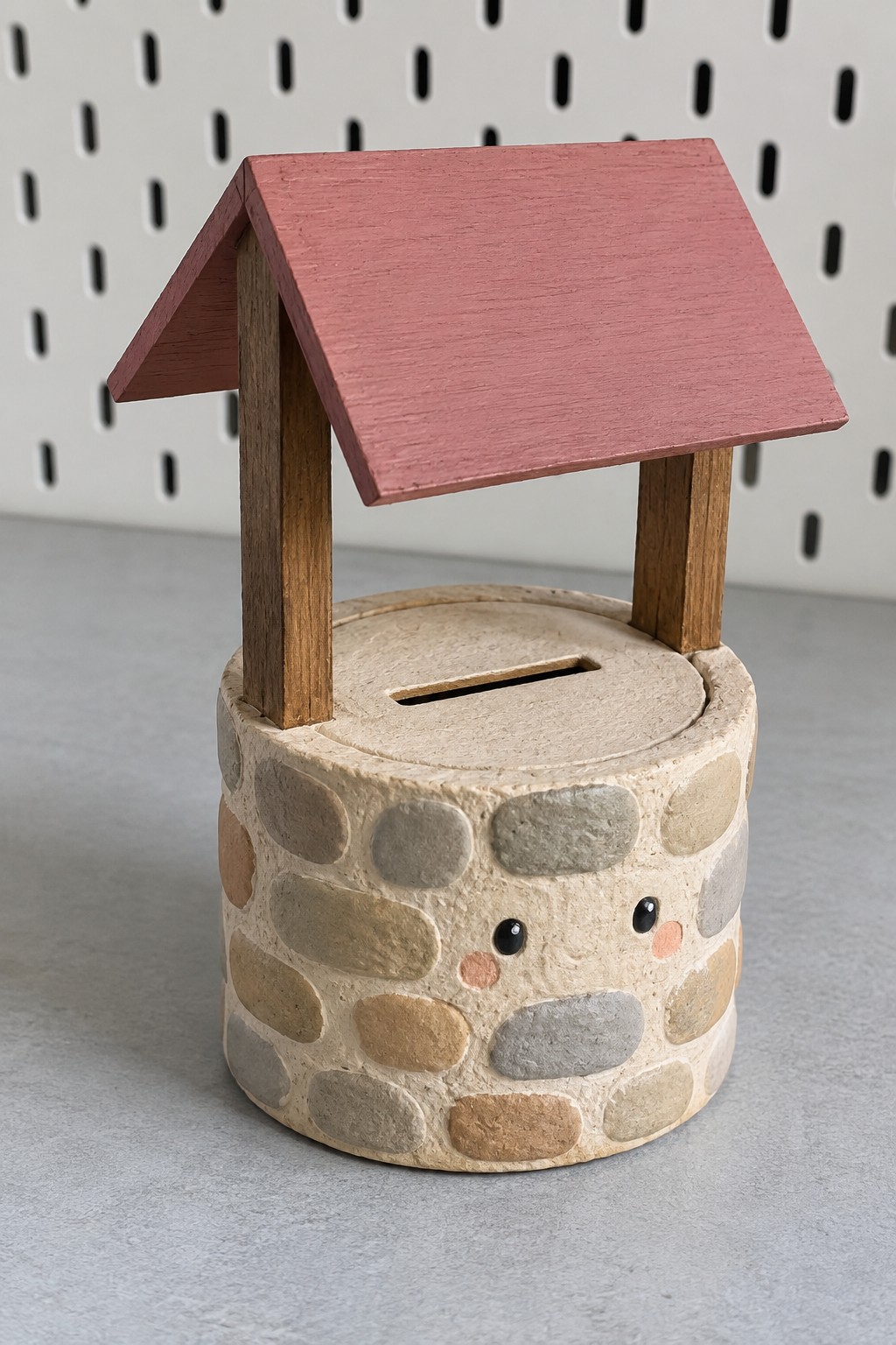 Round wishing well coin bank with painted stonework, a slotted lid, wooden posts and a dusty rose roof