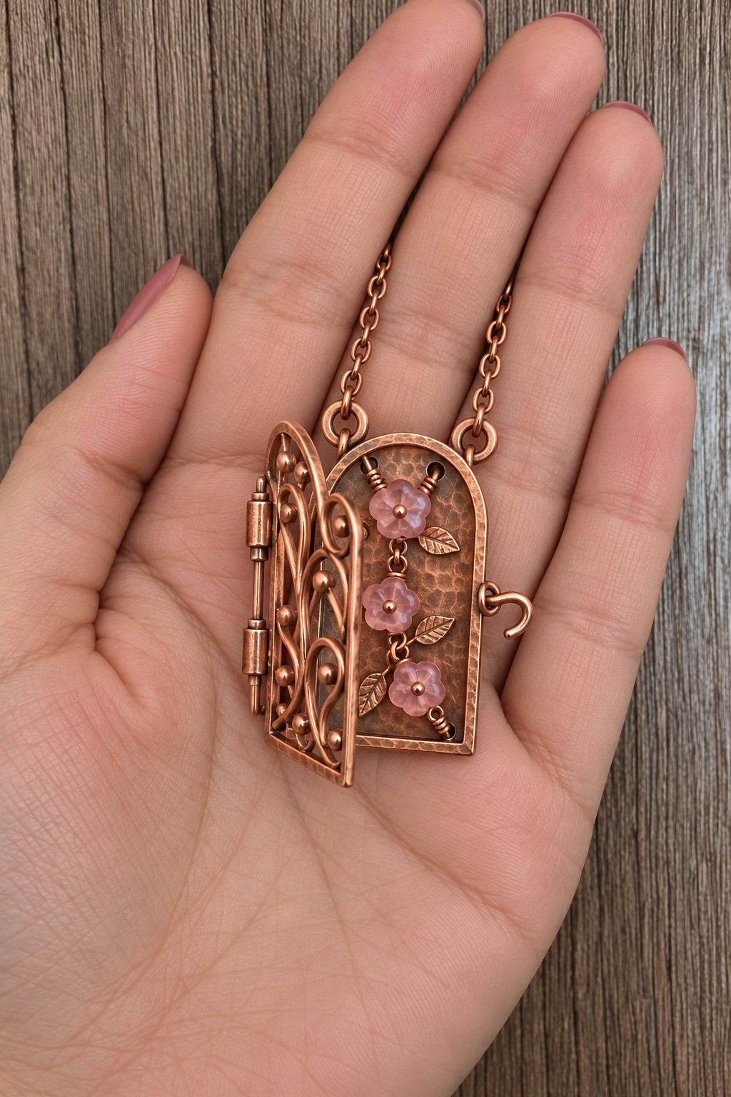 Arched copper pendant with an open filigree gate and three pink flowers inside