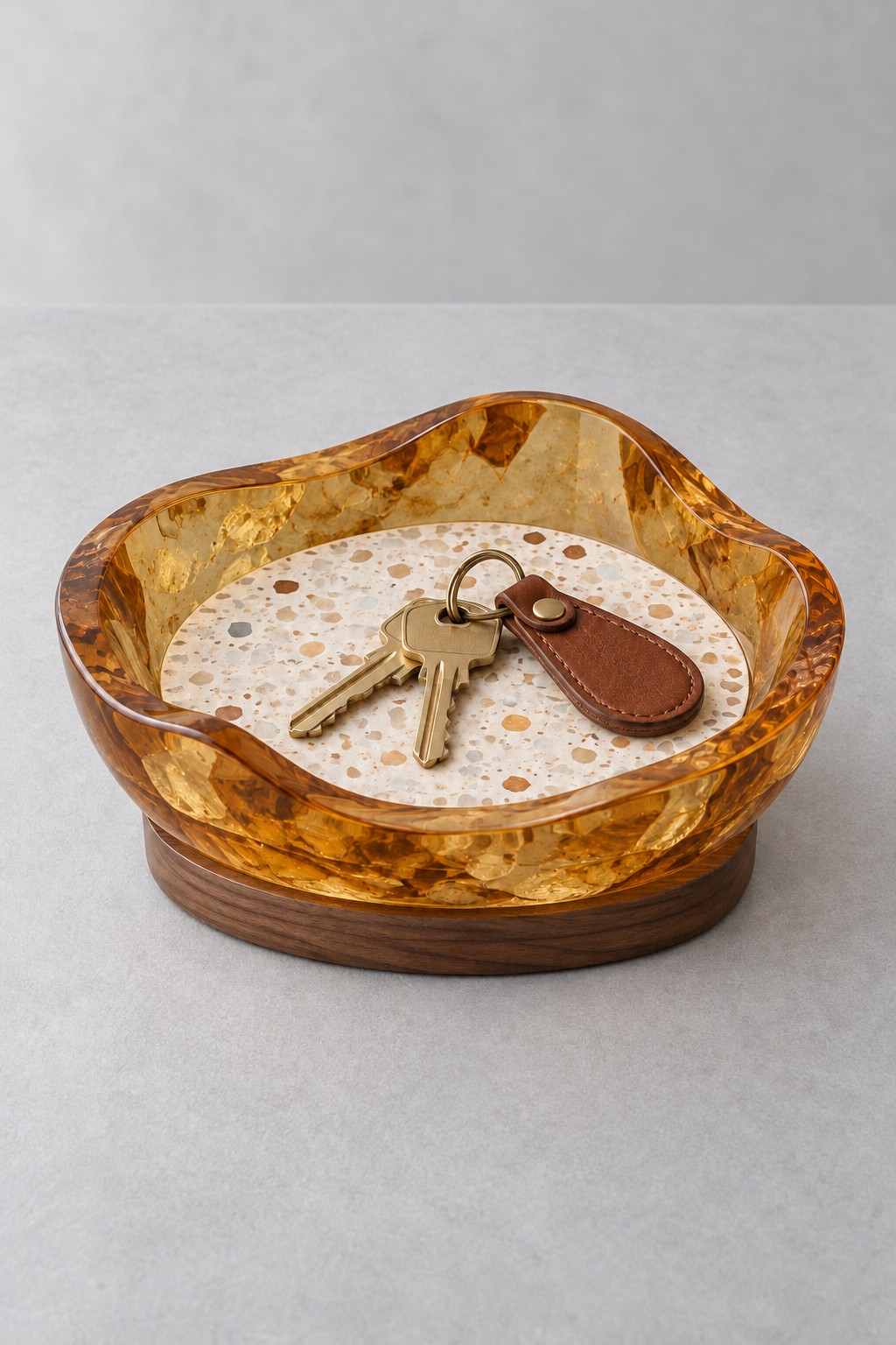 An amber resin catchall bowl with a wavy rim, round terrazzo style insert and wooden base, holding keys.